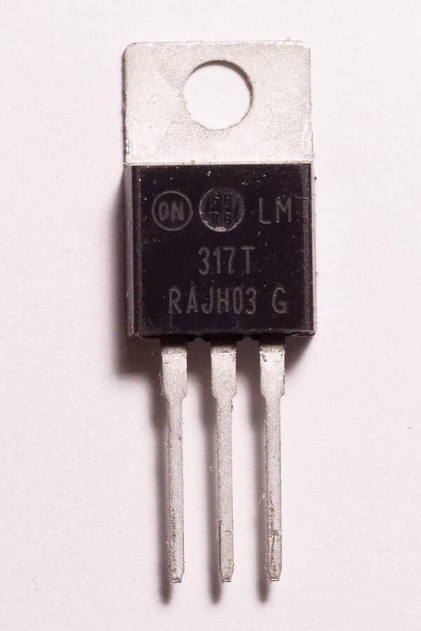 An LM317 adjustable voltage regulator in a black TO-220 package, showing its metal mounting tab and three thick legs.